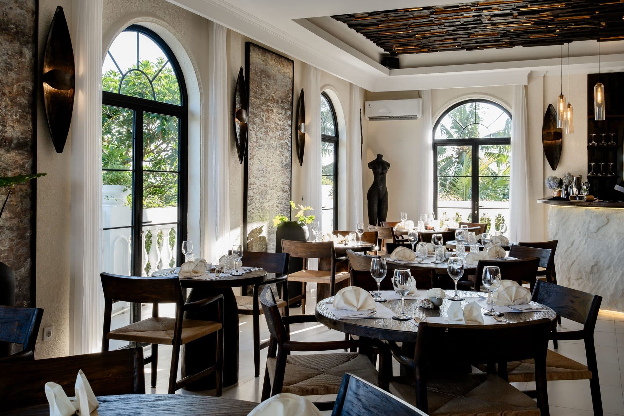 Round tables set with wine glasses and folded napkins in Kumo's dining room, under tall arched windows.