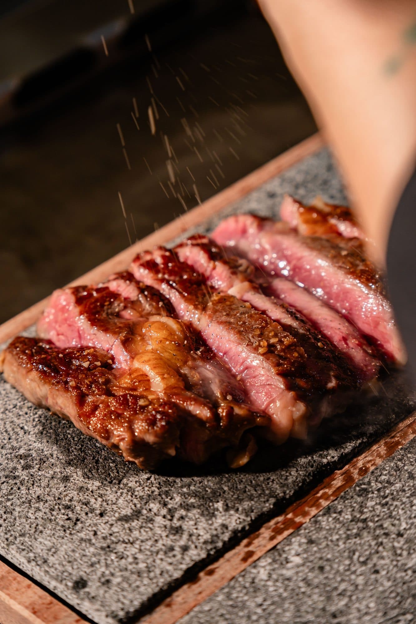 Sliced seared steak on a hot stone board at Kumo in Ubud, with seasoning falling onto the meat.